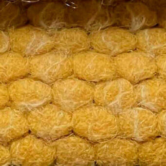 Puffo fabric sample, golden-yellow, densely woven with a fibrous, shredded texture in a honeycomb arrangement.